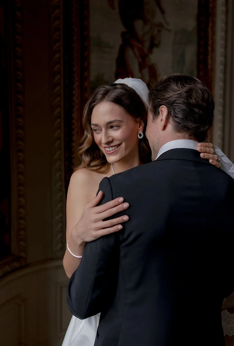 Ein Mann im schwarzen Anzug umarmt eine Frau in einem weissen Hochzeitskleid.