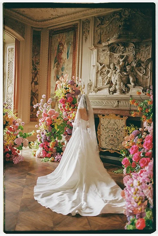 Eine Frau im Brautkleid steht in einem Raum der gefüllt ist mit bunten Blumen.