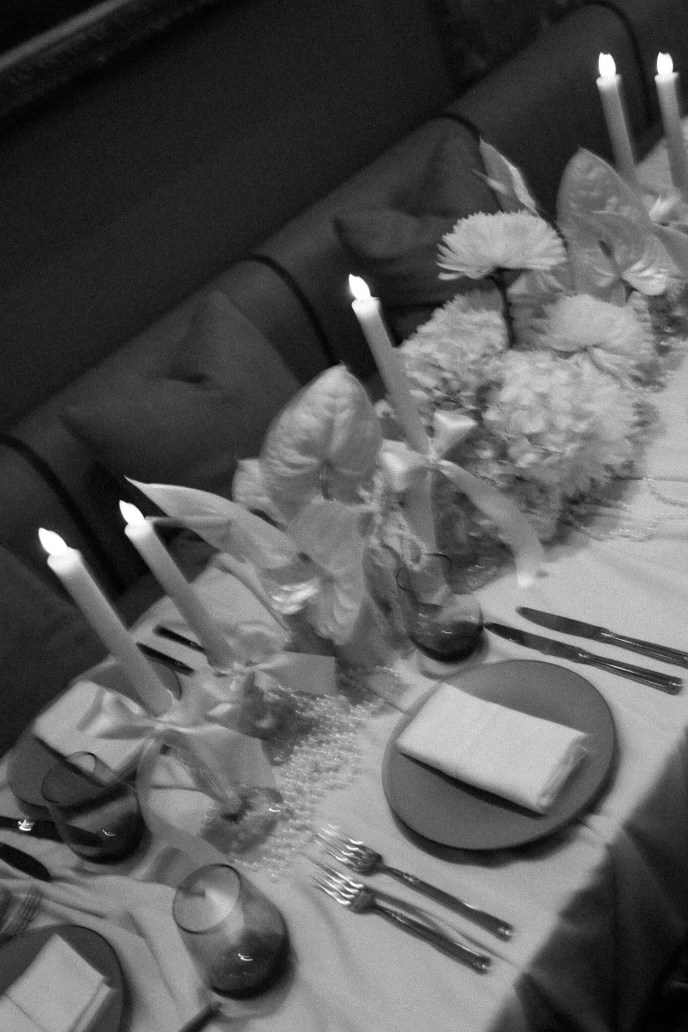 Ein eingedeckter Tisch mit weissen Blumen und Stabkerzen mit Maschen.