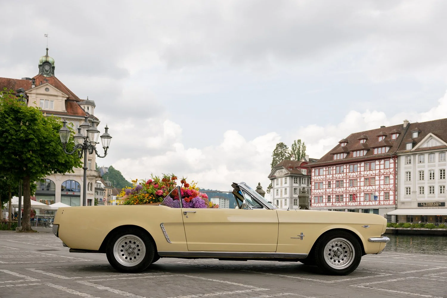Ein Hellgelber Oldtimer steht gefüllt mit bunten Blumen auf einem Platz in Luzern.