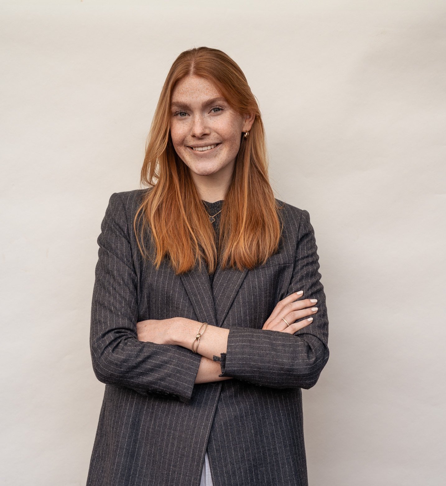 Eine Frau steht vor einer beigen Wand in einem grauen Blazer.