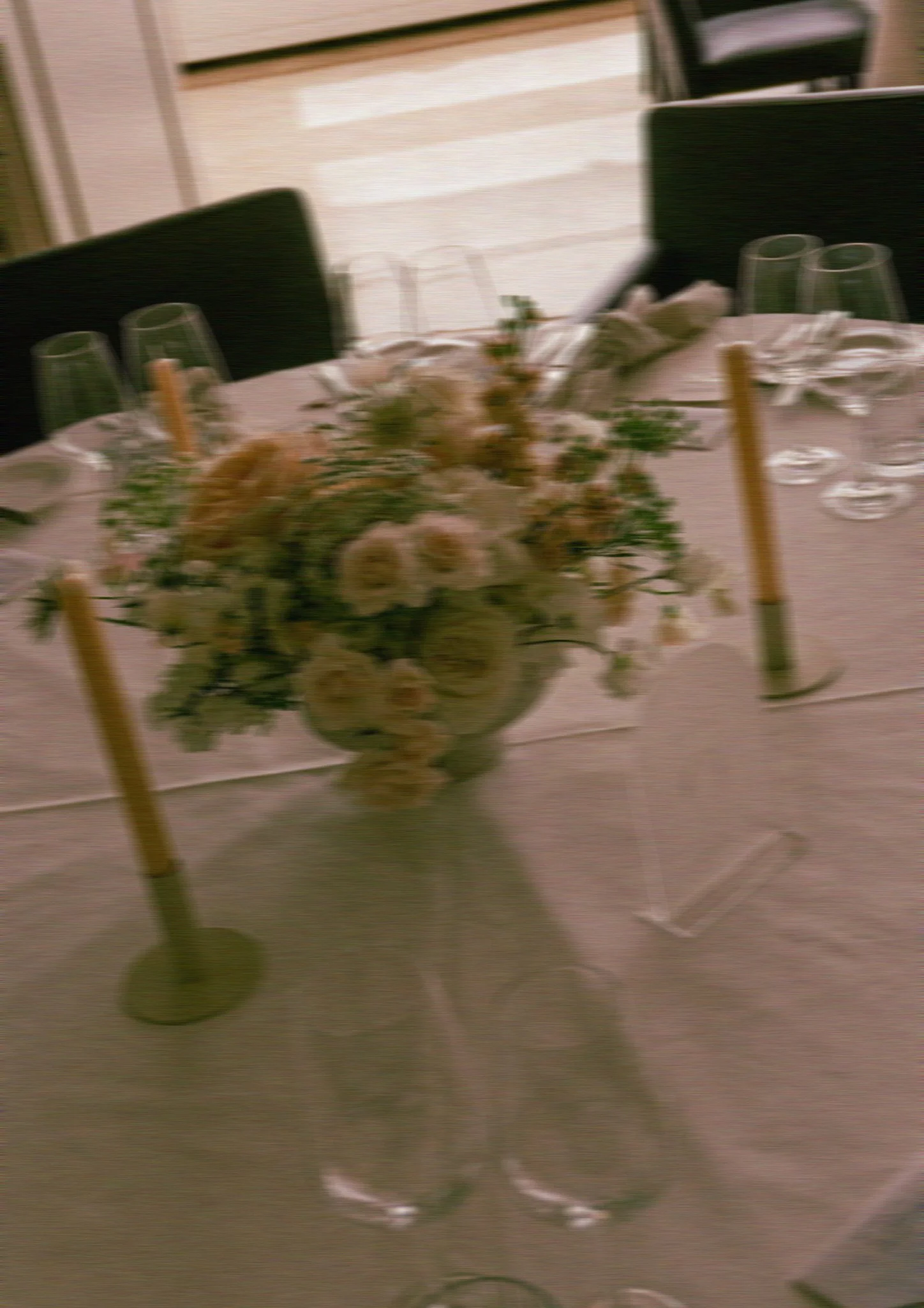 Ein Blumenbouquet in apricot Tönen steht in der Mitte eines Tisches mit Stabkerzen.