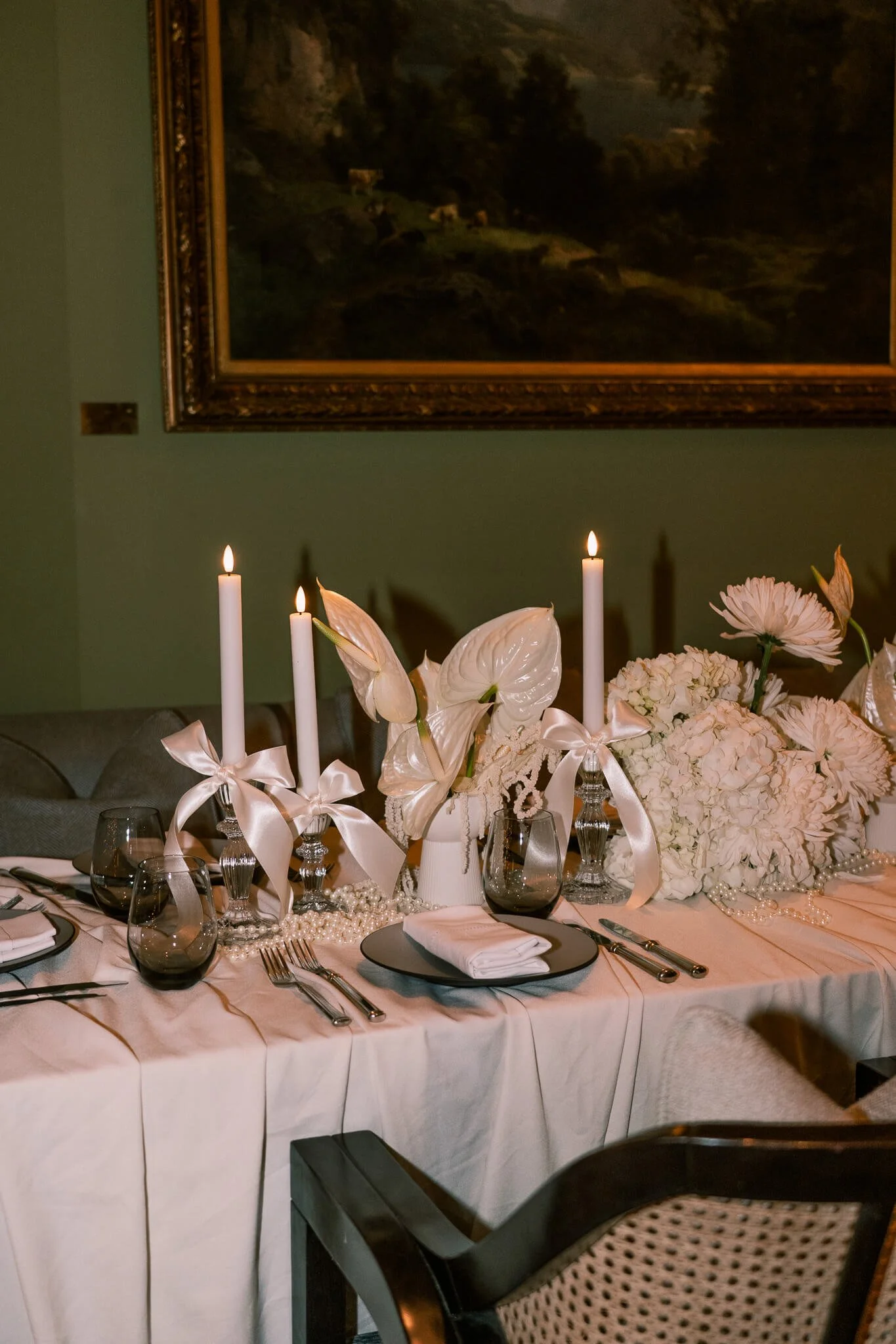 Ein eingedeckter Tisch ist dekoriert mit weissen Blumen und Stabkerzen mit weissen Maschen.