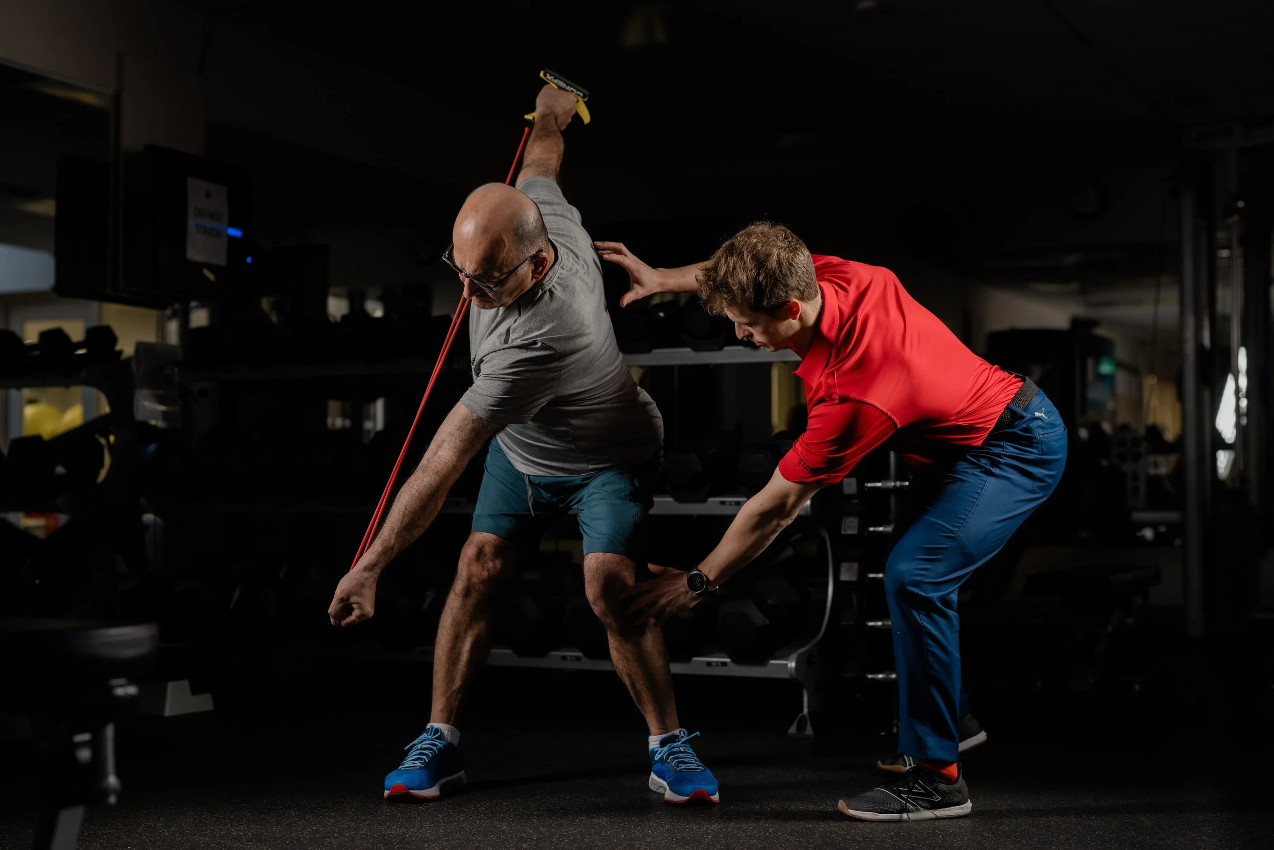 A fitness trainer assisting an older man with stretching exercises in a gym.