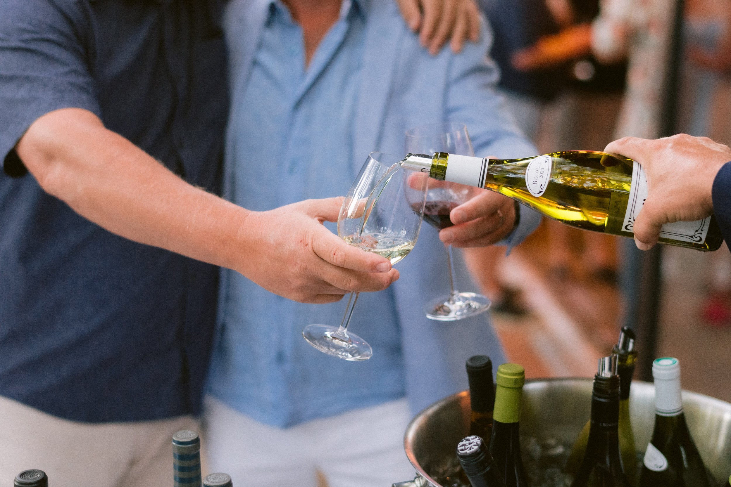 Person pouring white wine into a glass at a social gathering or event.