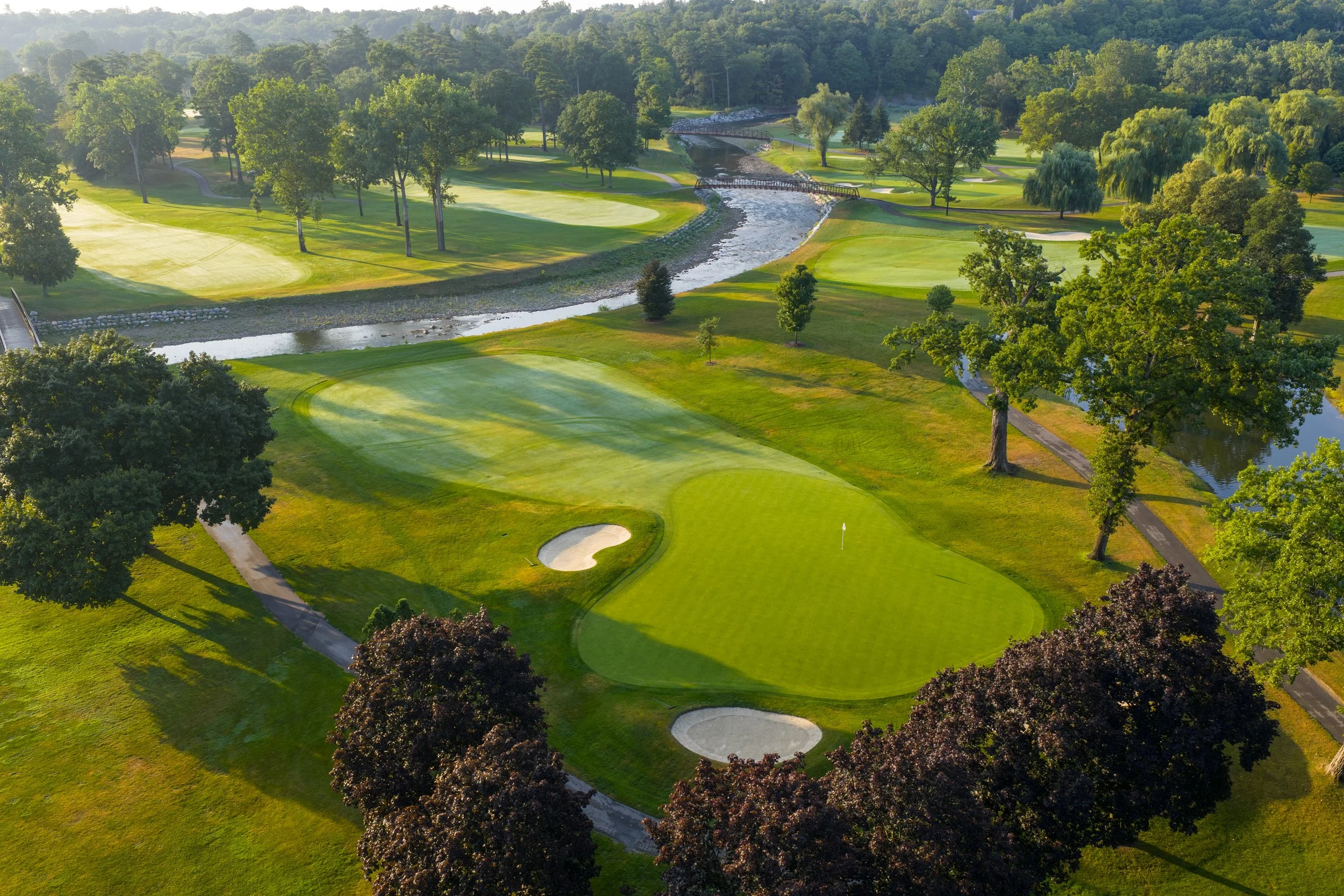 Aerial view of a golf course with green fairways, sand bunkers, trees, and Credit River with bridges.