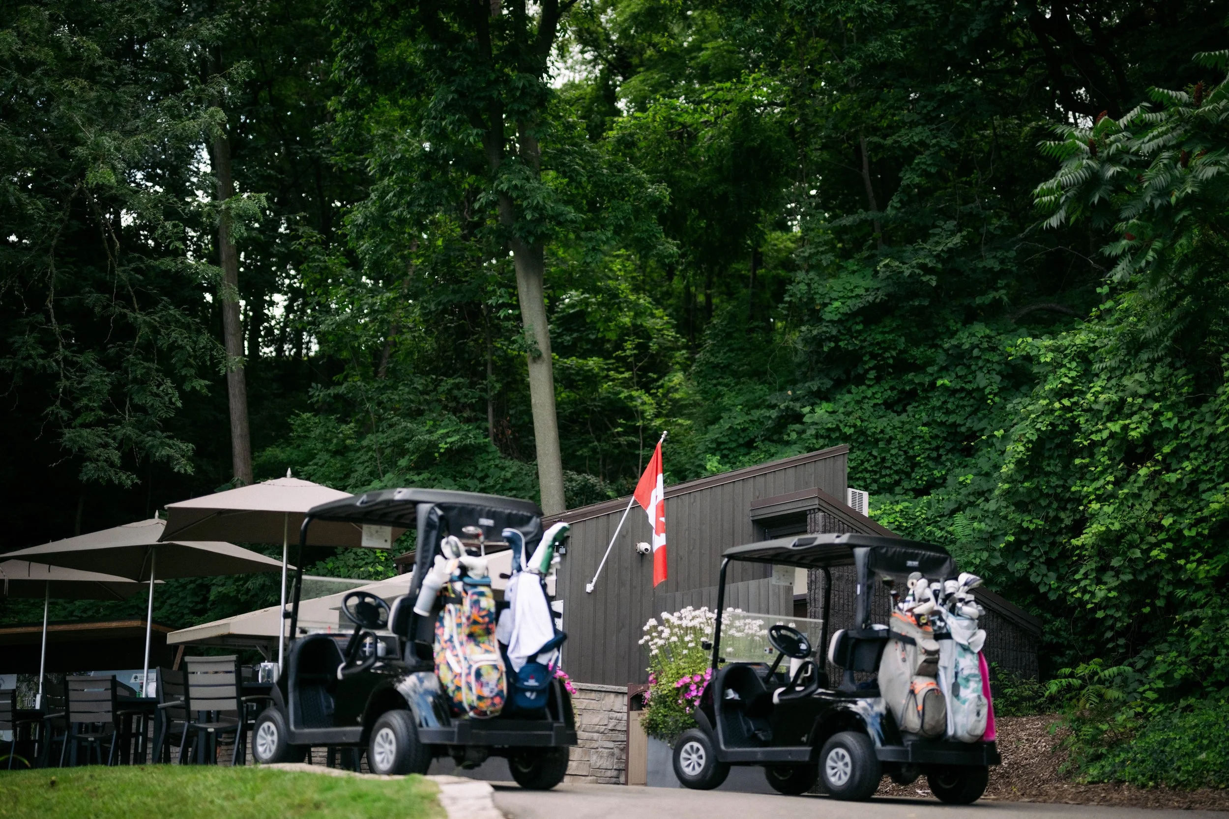Golf carts with golf bags parked near halfway house with patio umbrellas and a wooded background.
