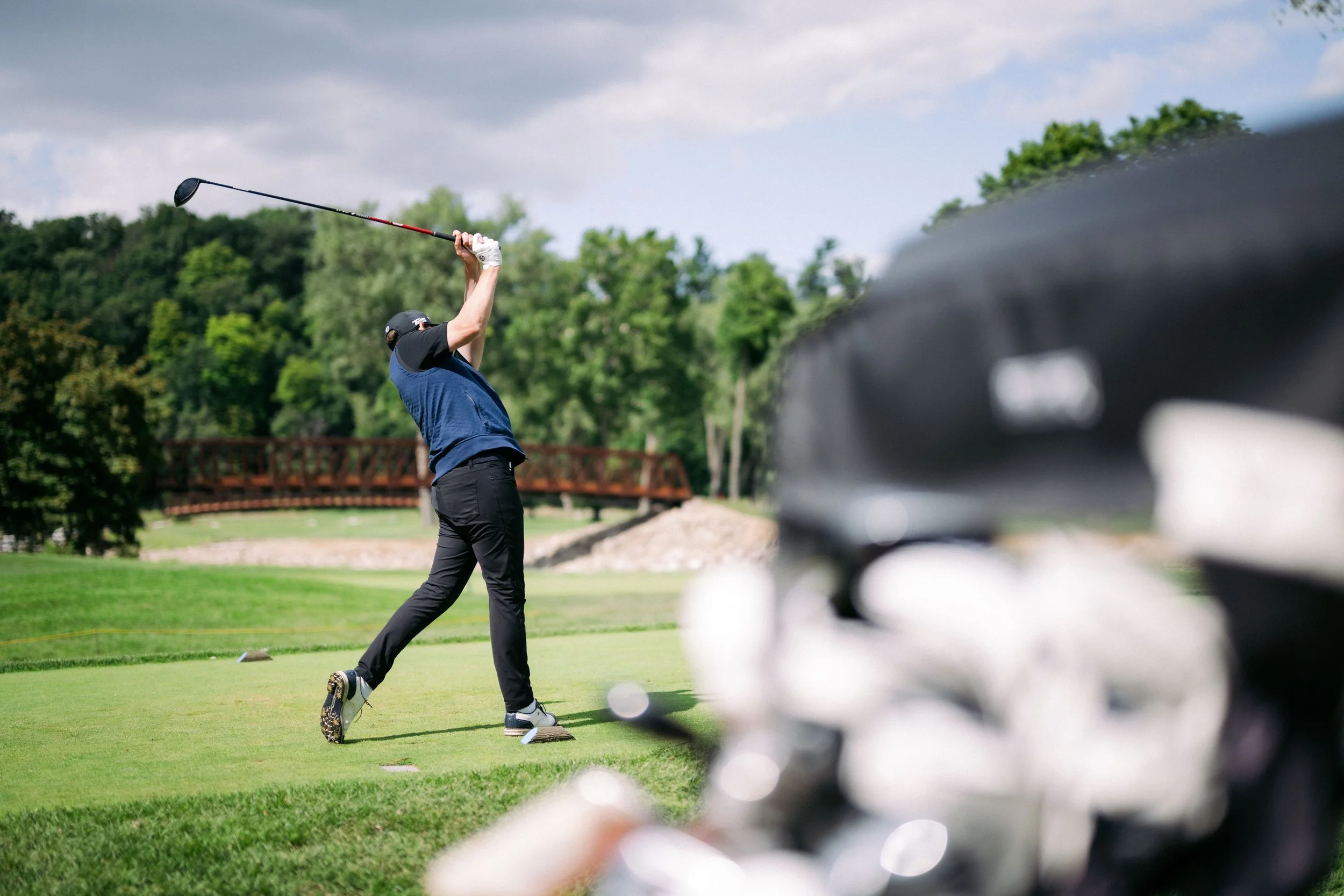 A man hitting a golf ball on a golf course, with golf clubs in a bag in the foreground.