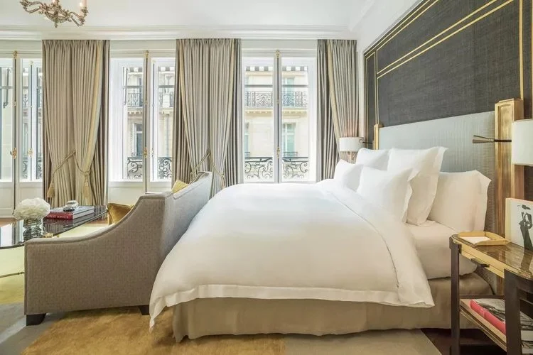 Luxurious hotel room with a large bed, elegant sofa, floor-to-ceiling windows, and opulent decor.