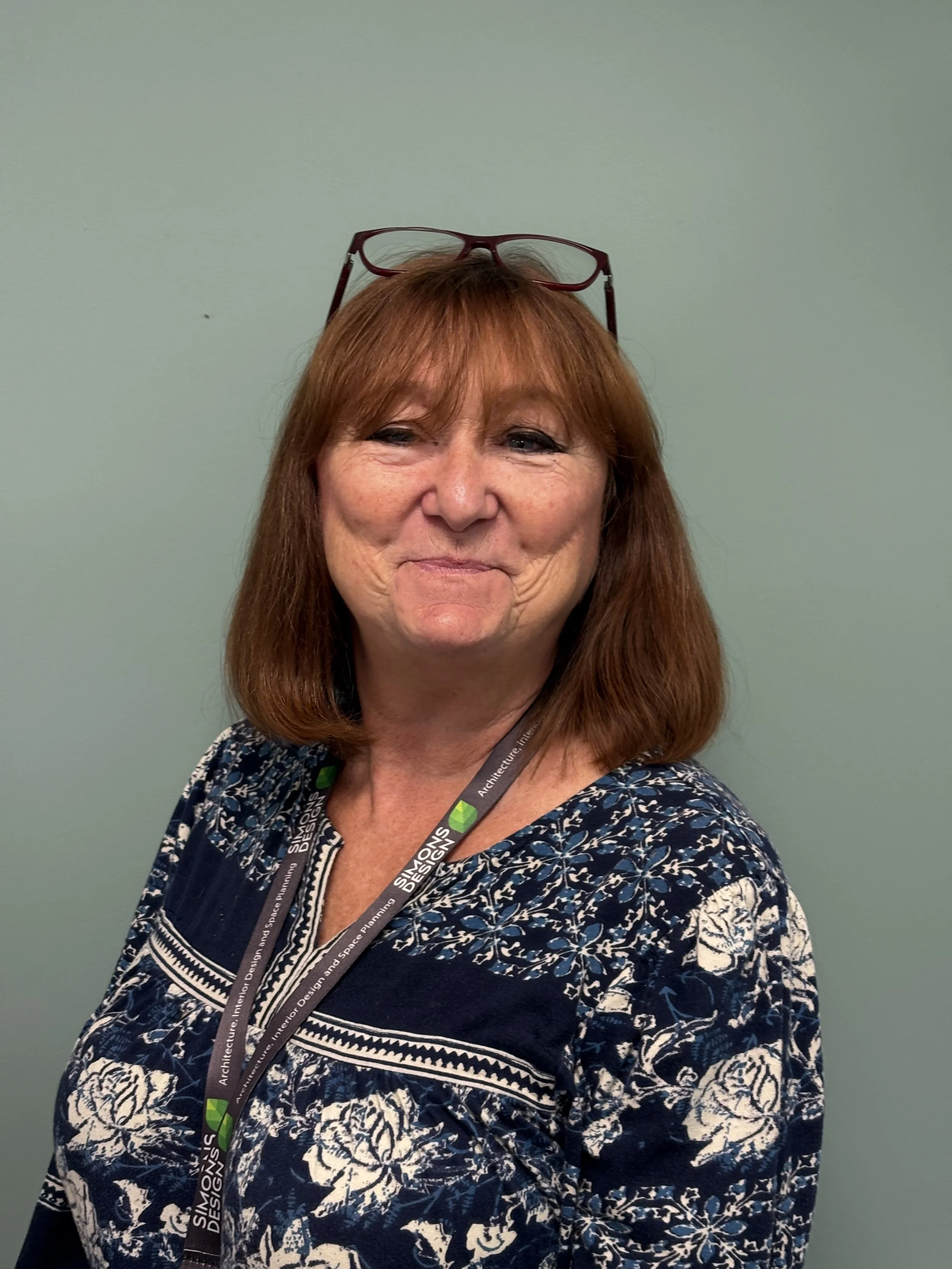 Smiling woman in a polka dot dress seated against a green background.