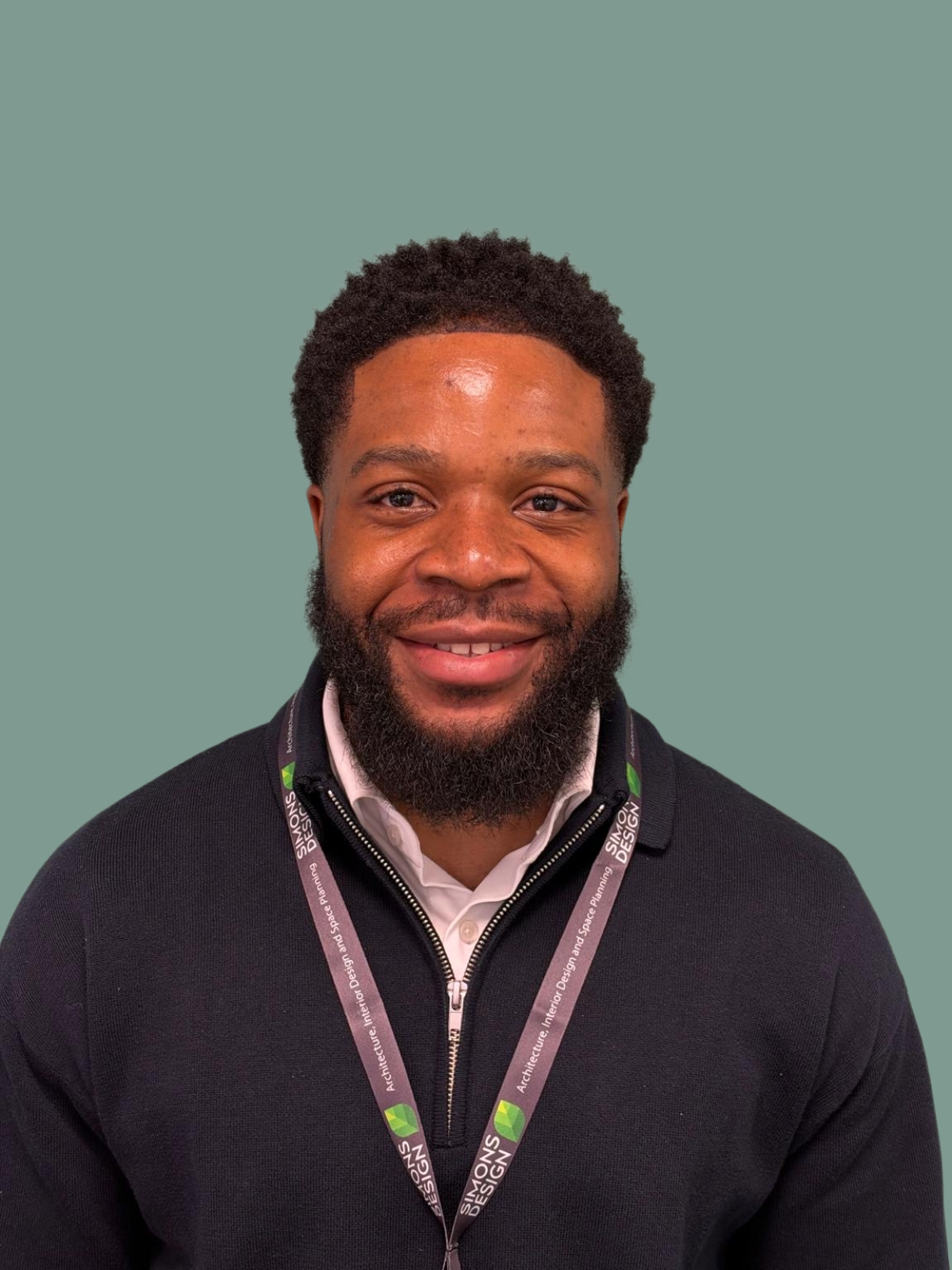 Portrait of a man with glasses and a beard wearing a green blazer and blue shirt against a green background.