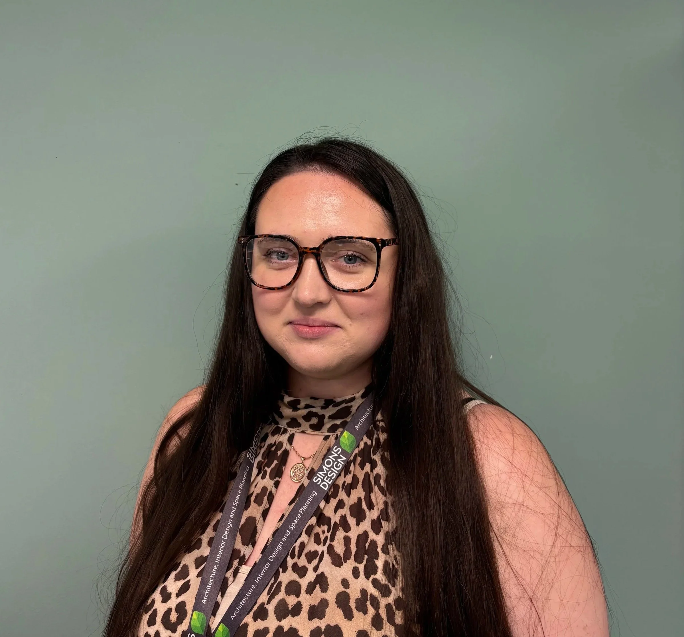 Portrait of a woman with glasses and long dark hair smiling against a green background.