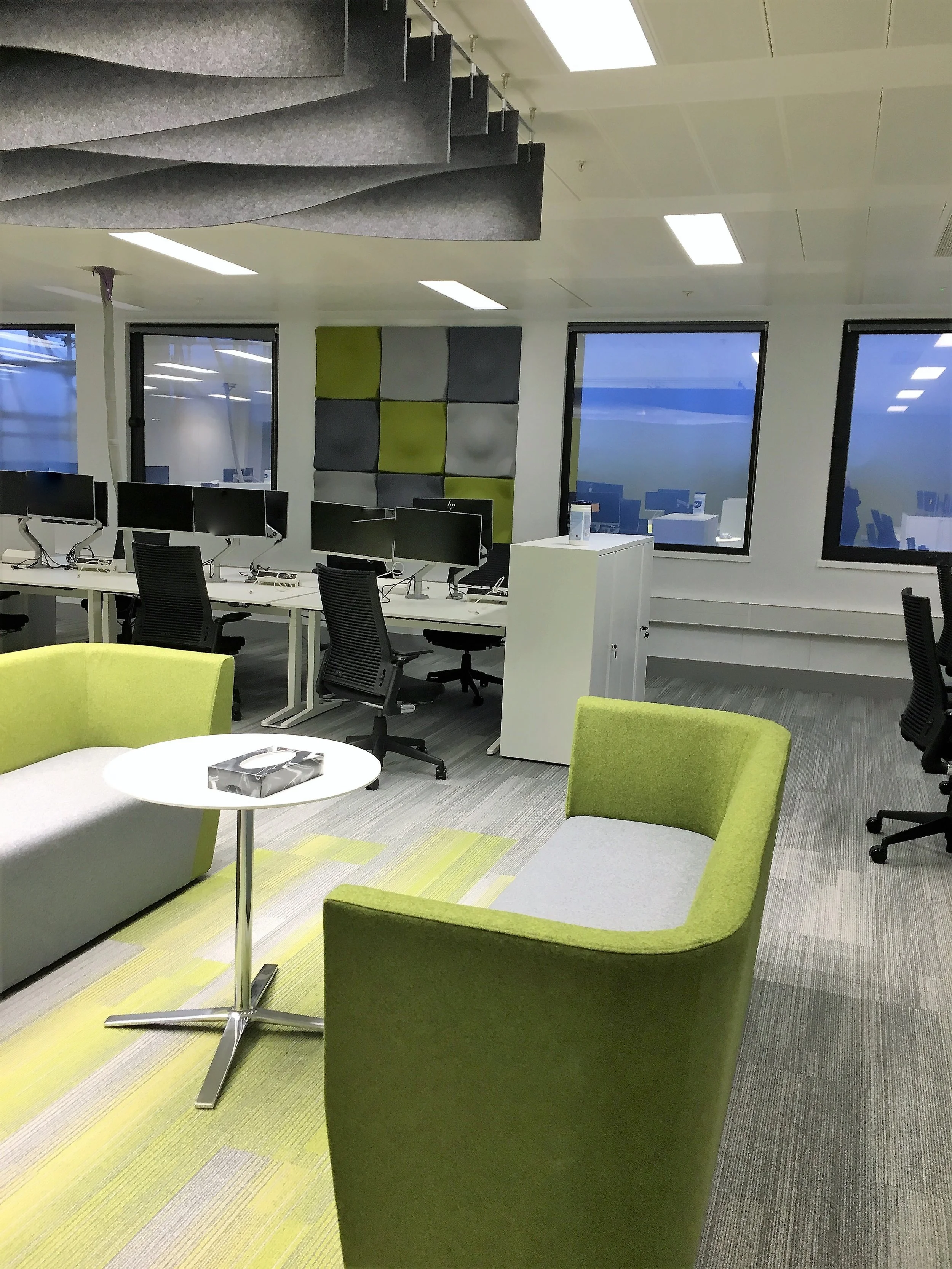 Modern office interior with green and gray furniture, workstations, and acoustic ceiling design.