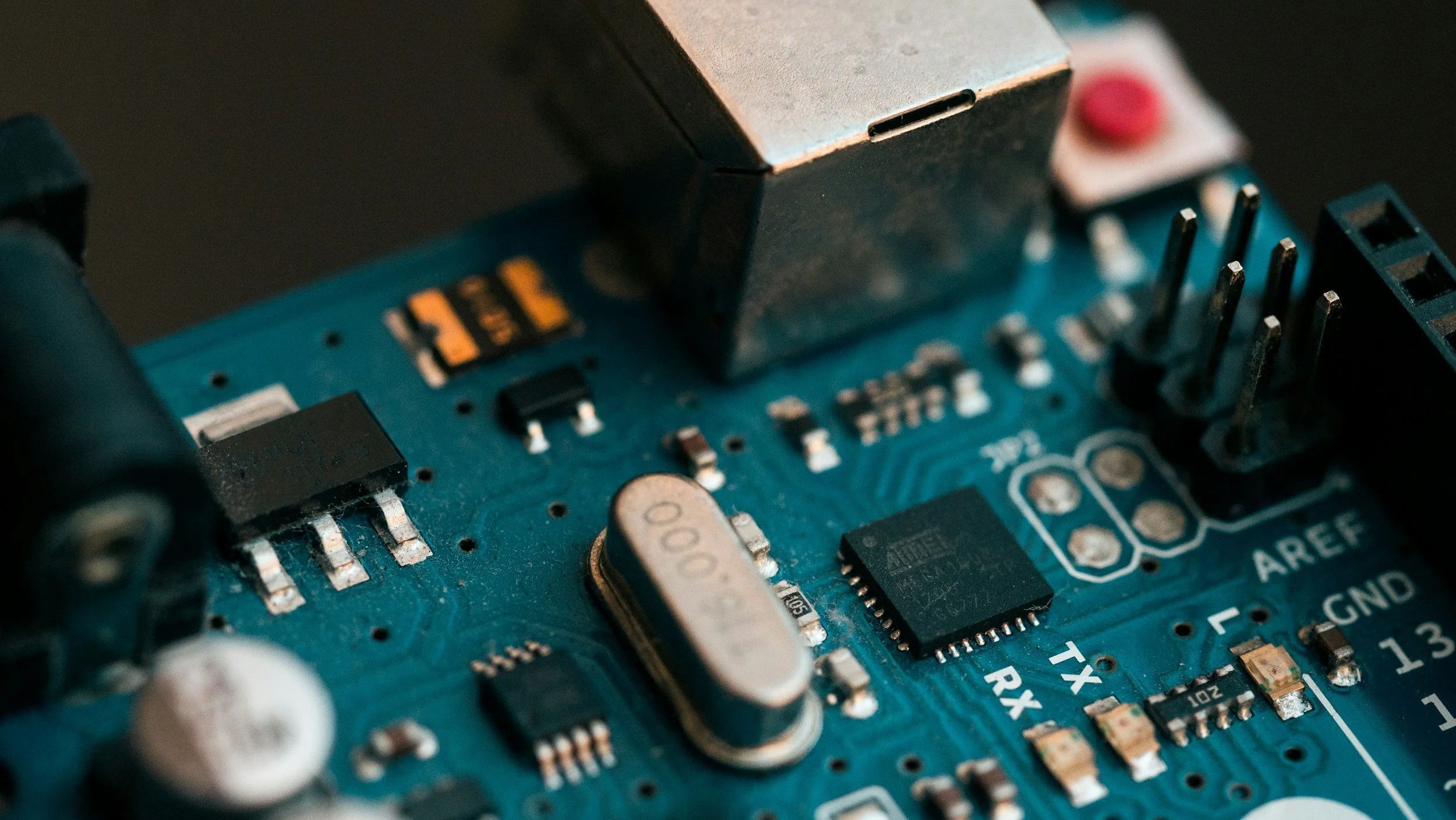 Close-up of a blue printed circuit board with various electronic components, including an integrated circuit, resistors, capacitors, and pin headers.