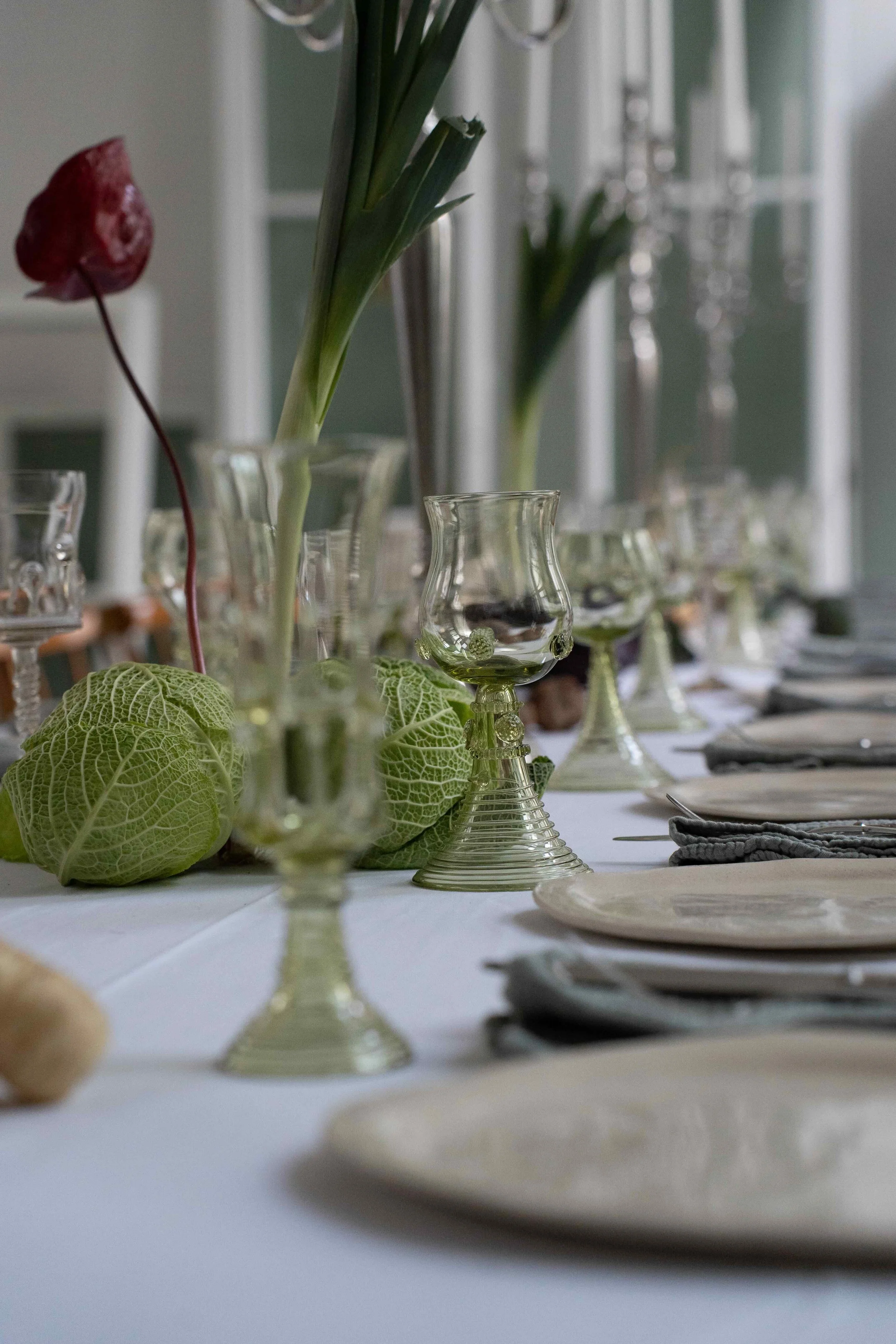 Elegant dining table setting with decorative cabbages, wine glasses, and white plates on a tablecloth