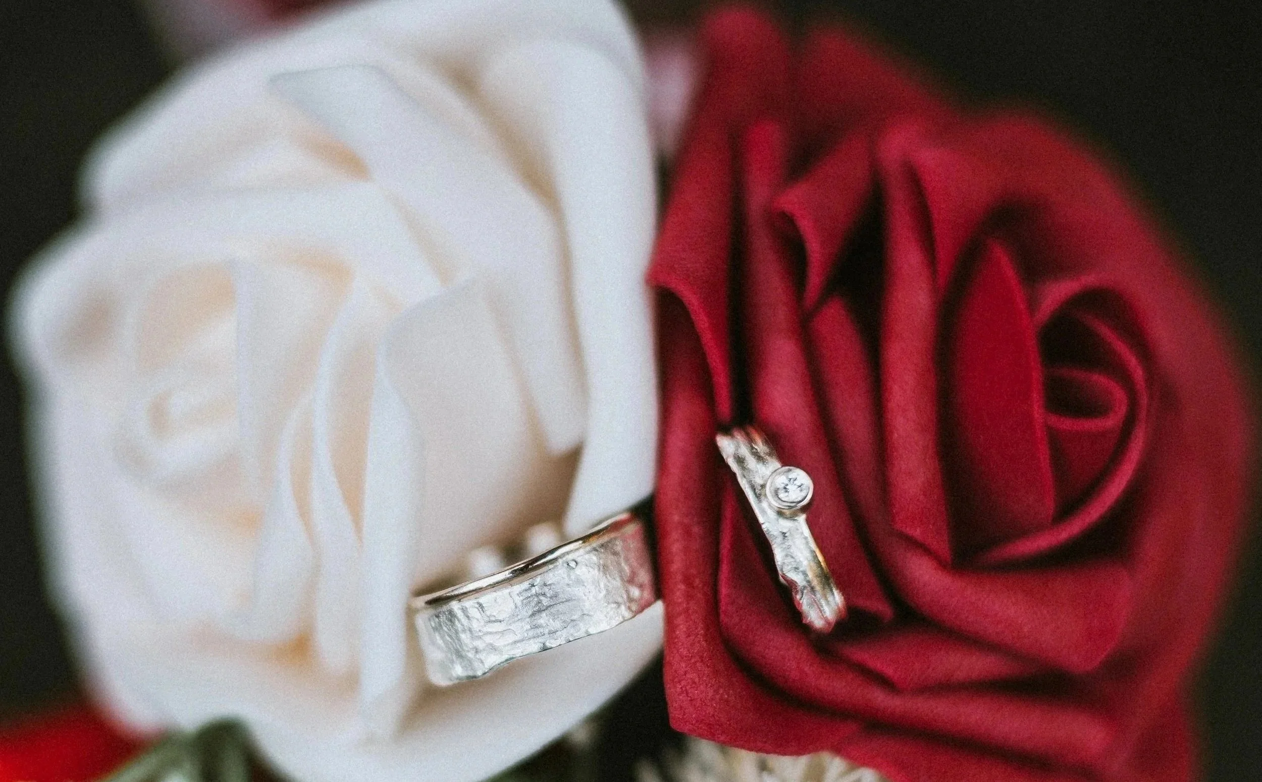 Een close-up van een zilveren trouwring met een grote diamant, geplaatst op een rode stof, naast een witte bloem voor een bruiloft