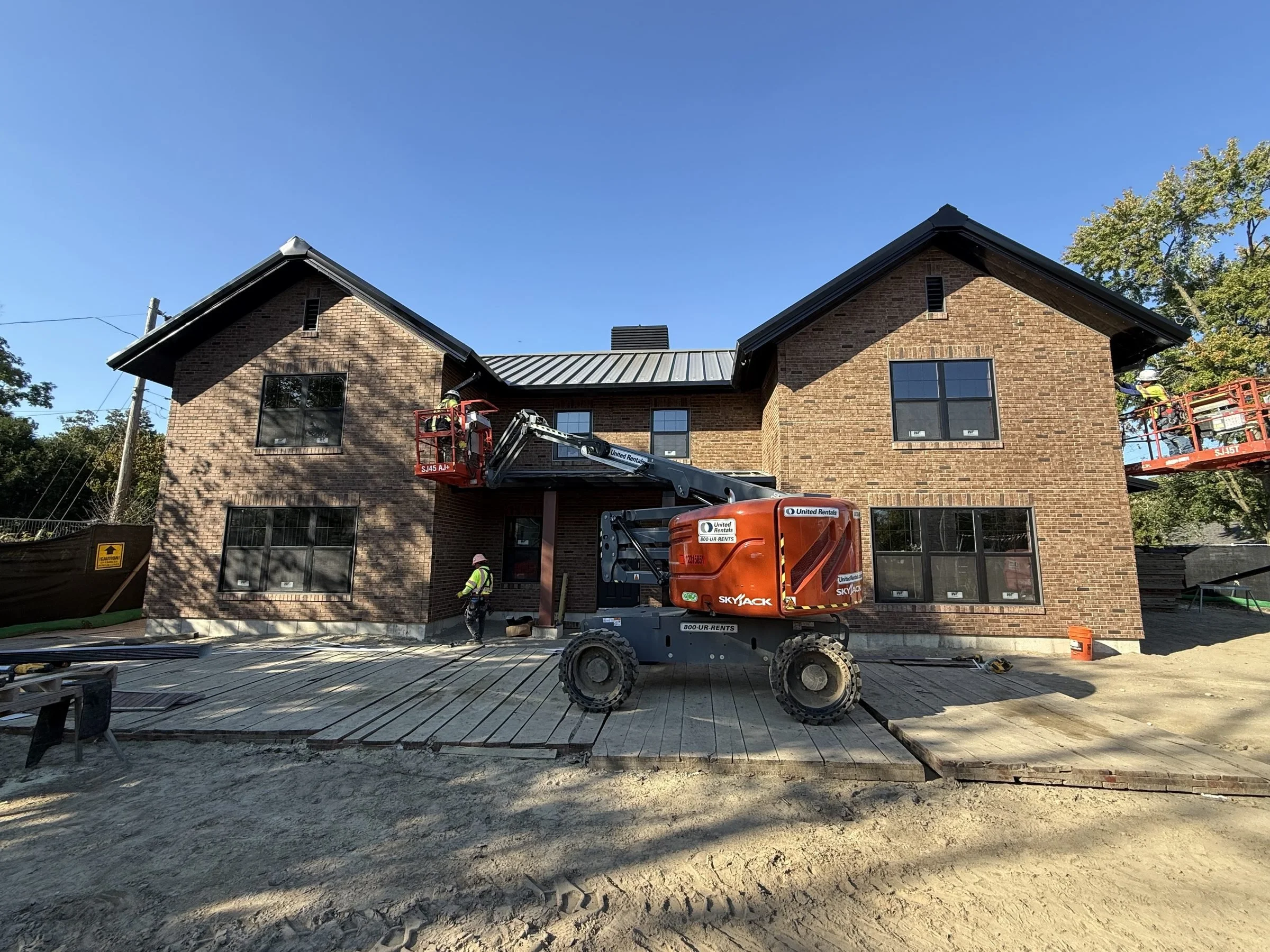 Construction workers using orange Skyjack lifts to renovate a brick building under a clear blue sky