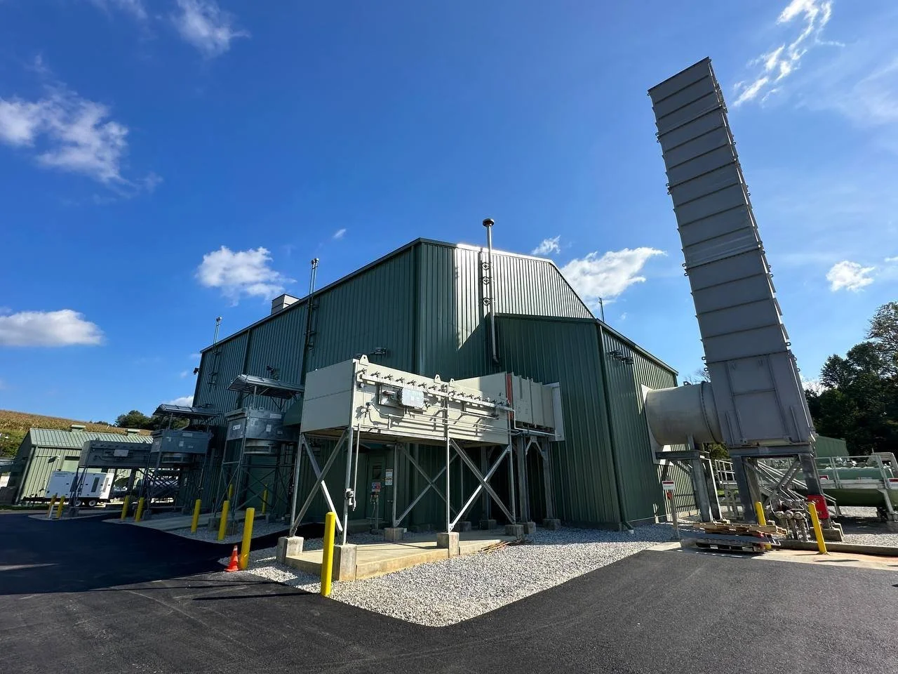 Industrial processing facility with green metal buildings, conveyors, exhaust ducts, and equipment under a blue sky