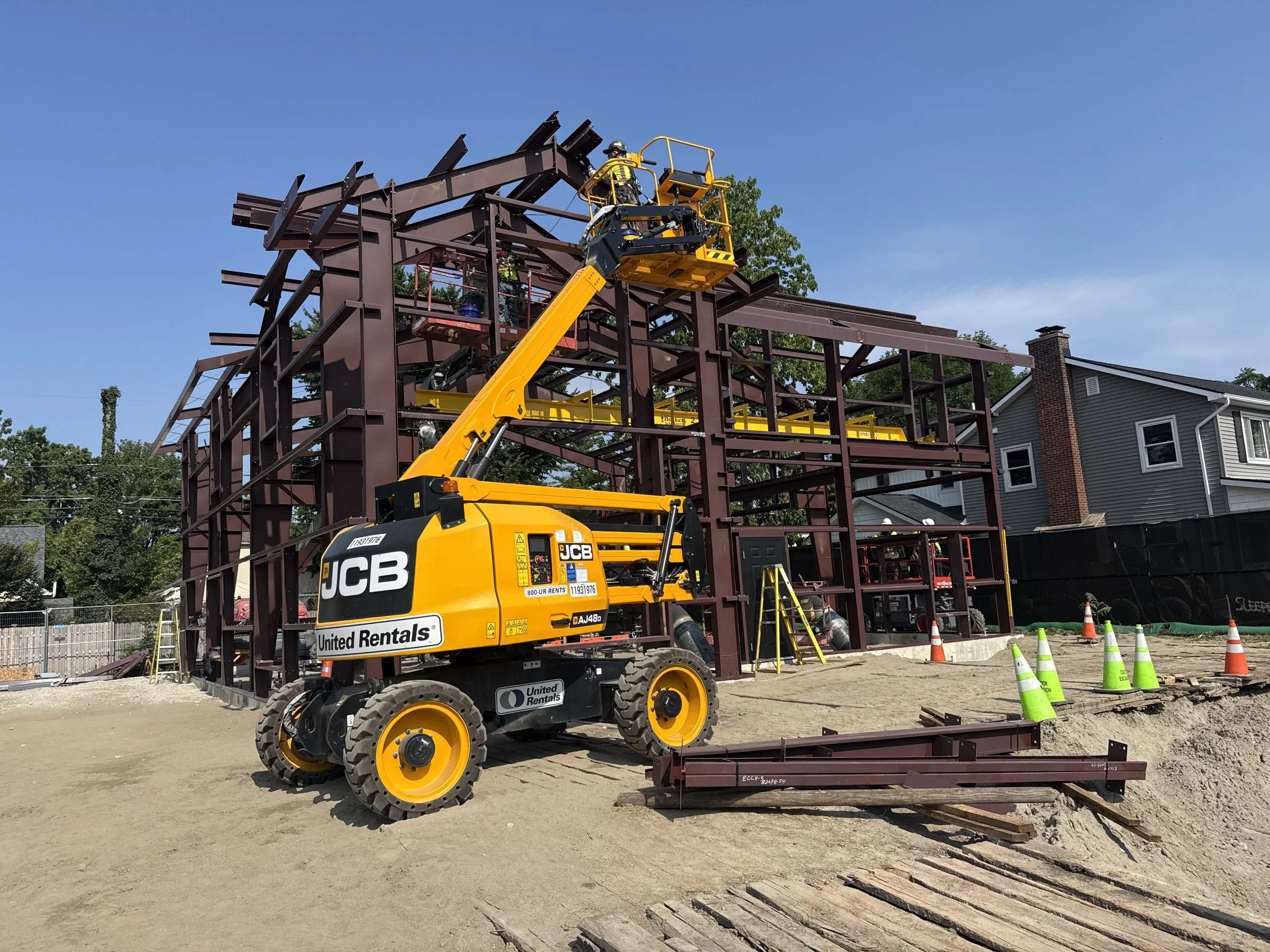 Boom lift with workers constructing a steel-framed building at a sunny construction site