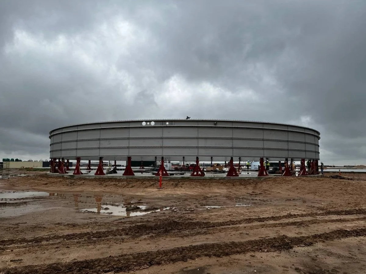 Large cylindrical industrial biogas tank under construction at a muddy construction site on a cloudy day