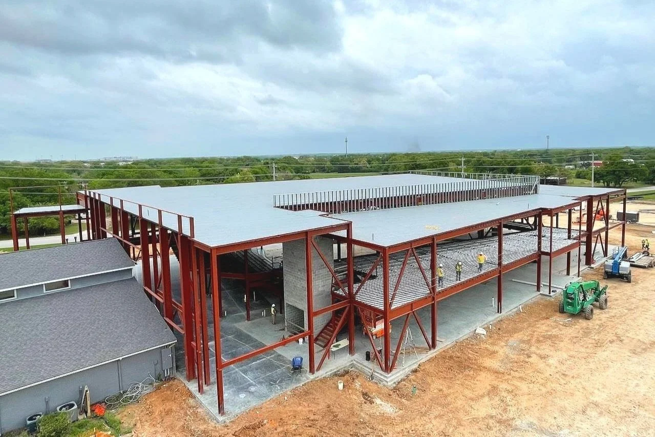 Aerial view of a large steel-frame commercial building under construction with workers and heavy equipment.