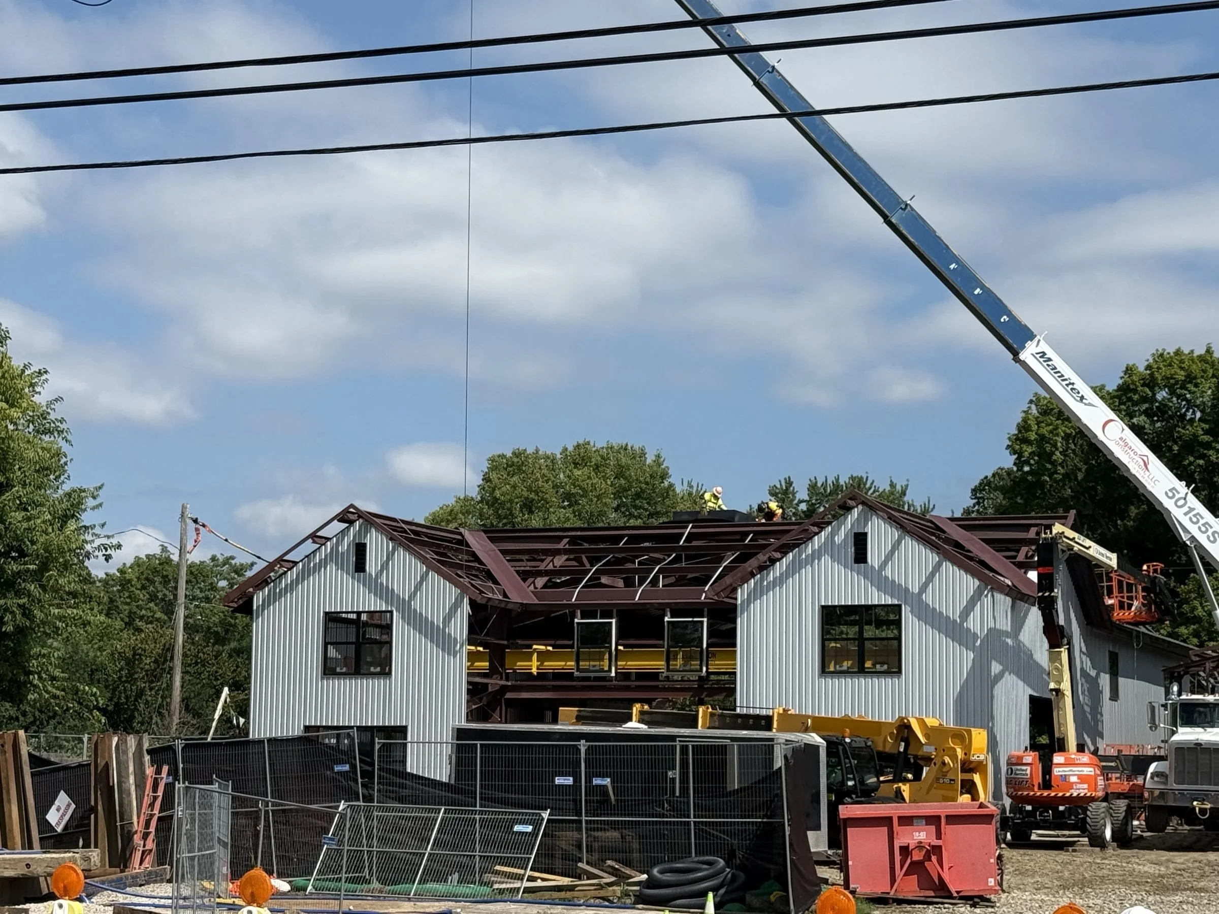 Construction workers and heavy equipment renovate a large metal-sided building beneath a telescopic crane.