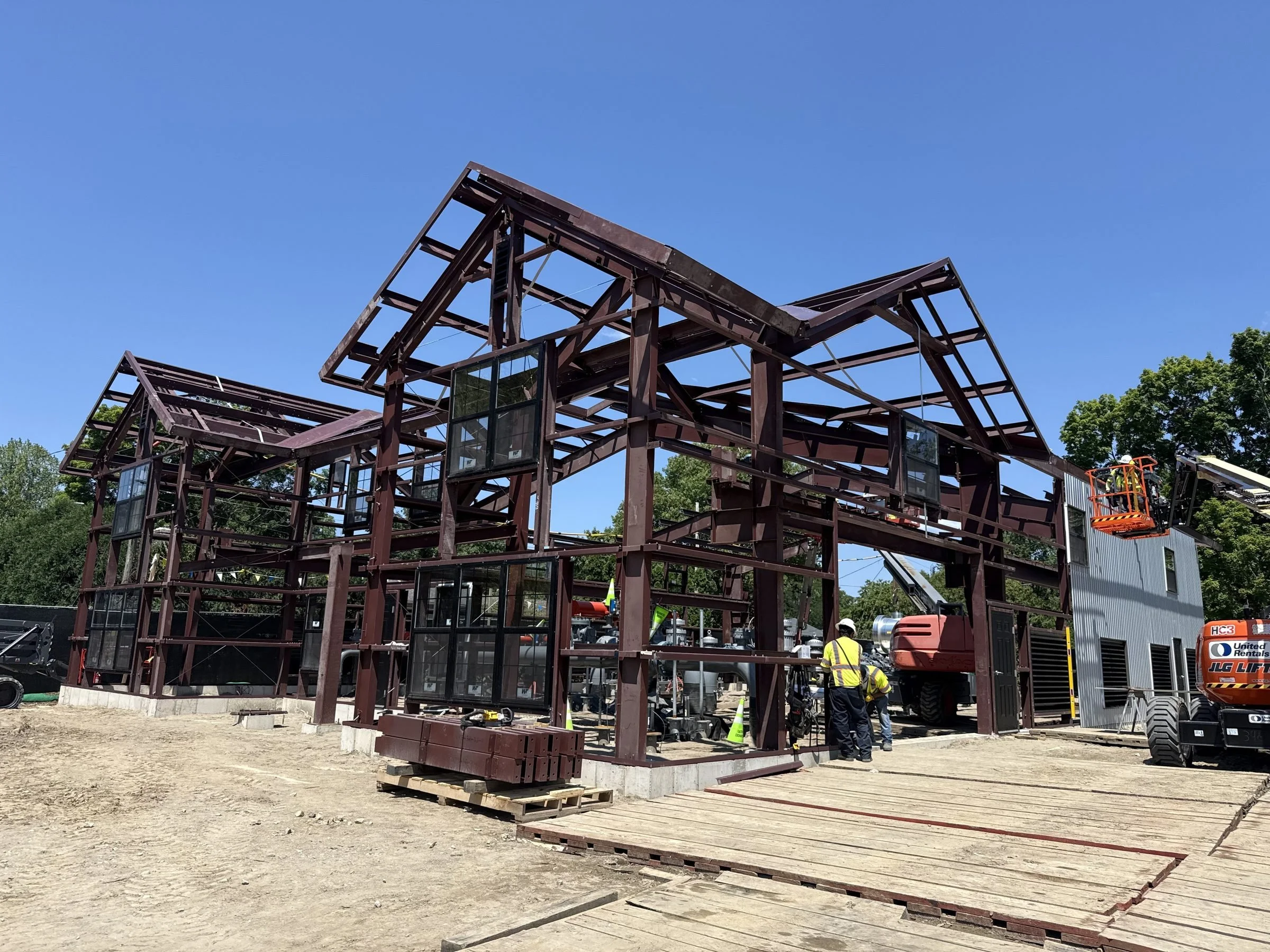 Construction workers assembling a large steel-framed building with lifts at an outdoor construction site
