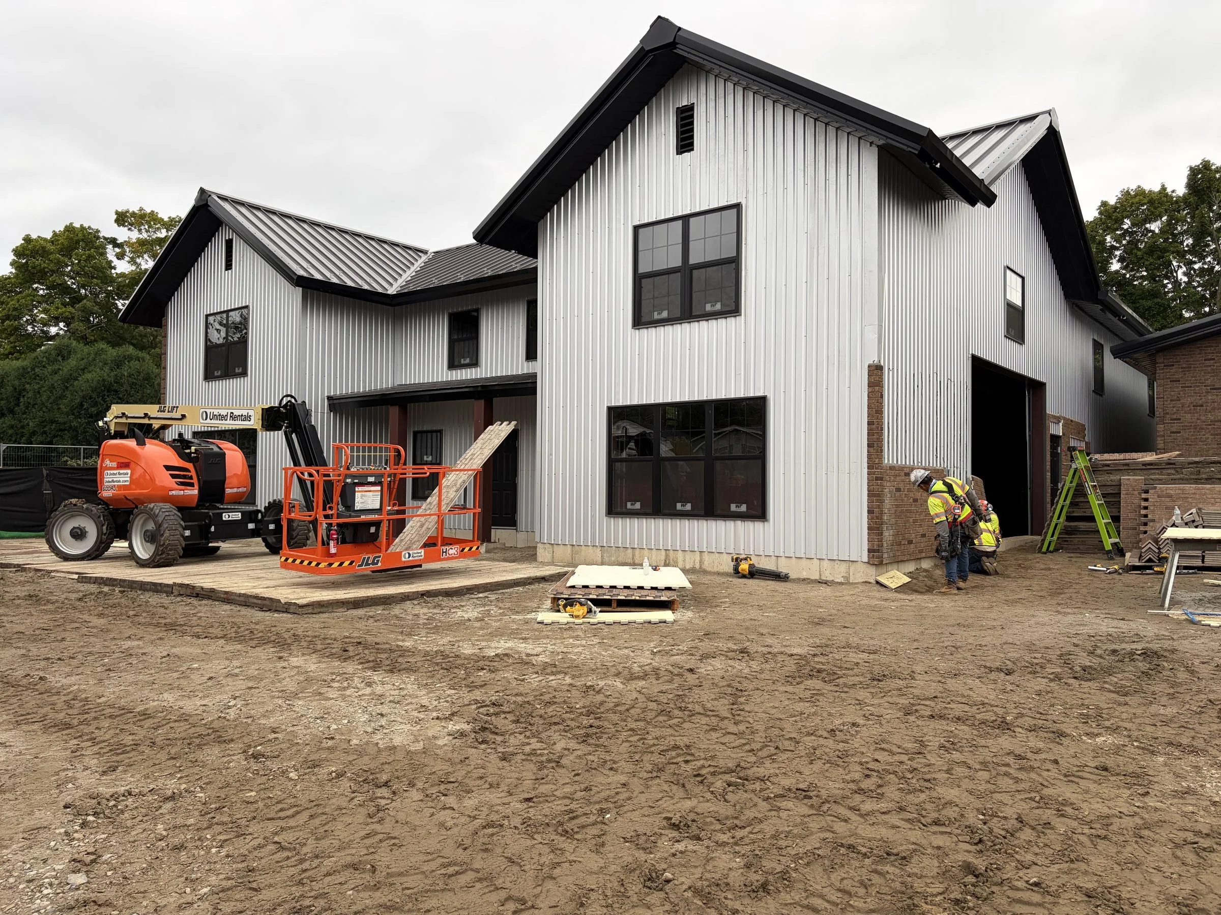 Construction workers and lifts outside a modern metal-sided building under construction