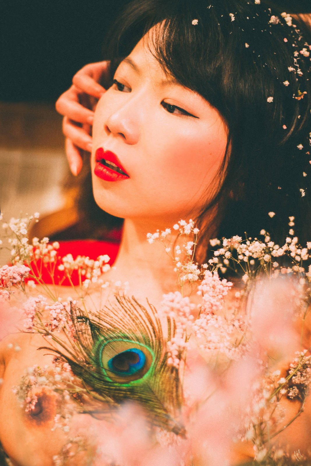 Artistic portrait of a woman surrounded by baby's breath flowers and a peacock feather, with elegant makeup and styled hair.