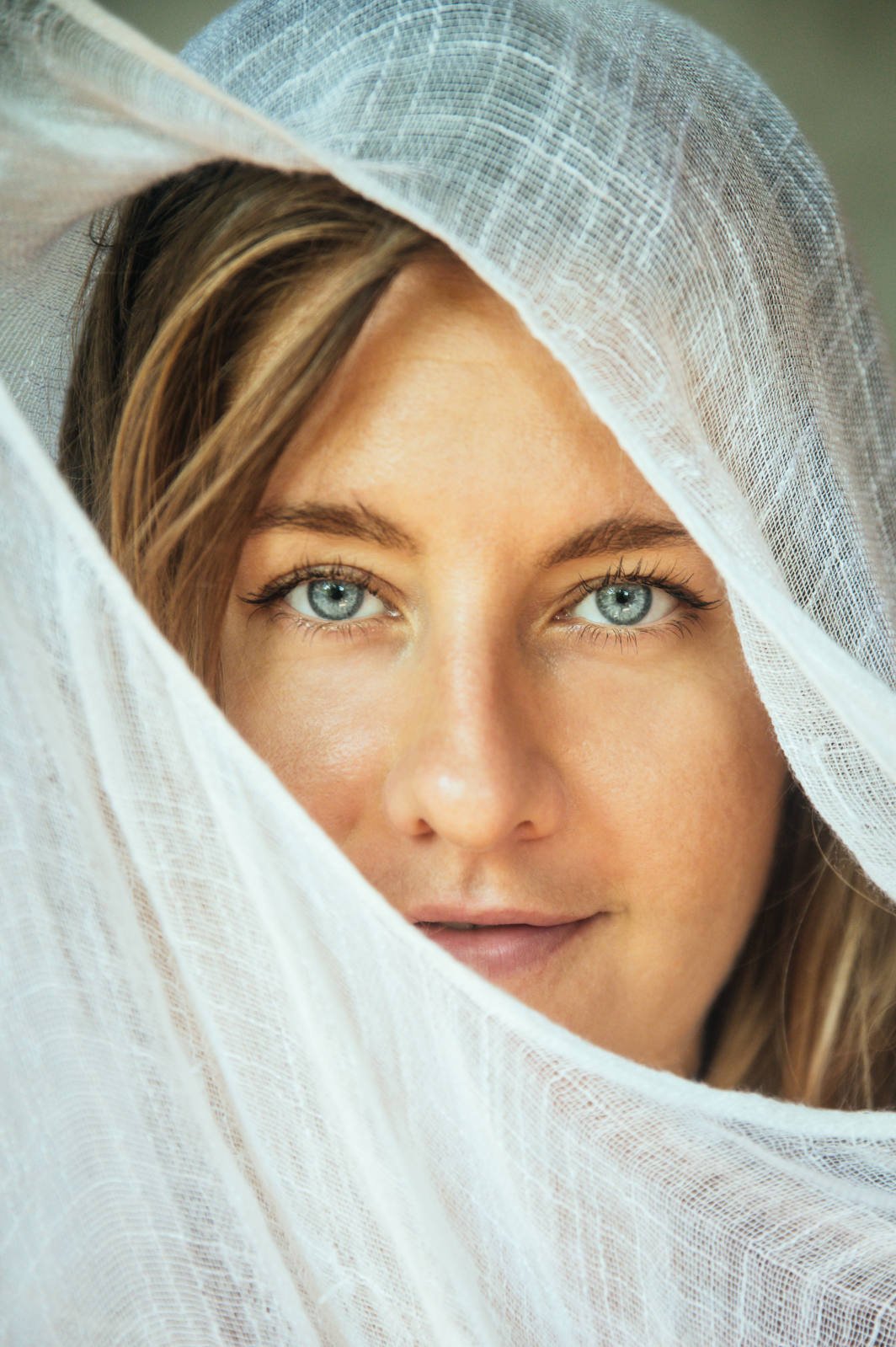 Close-up of a woman with blue eyes partially covered by a white sheer fabric.