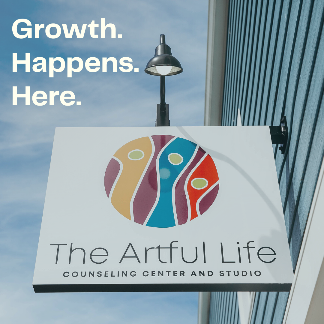 Sign for The Artful Life Counseling Center and Studio with a colorful abstract logo, mounted outside under a light fixture on a blue building.