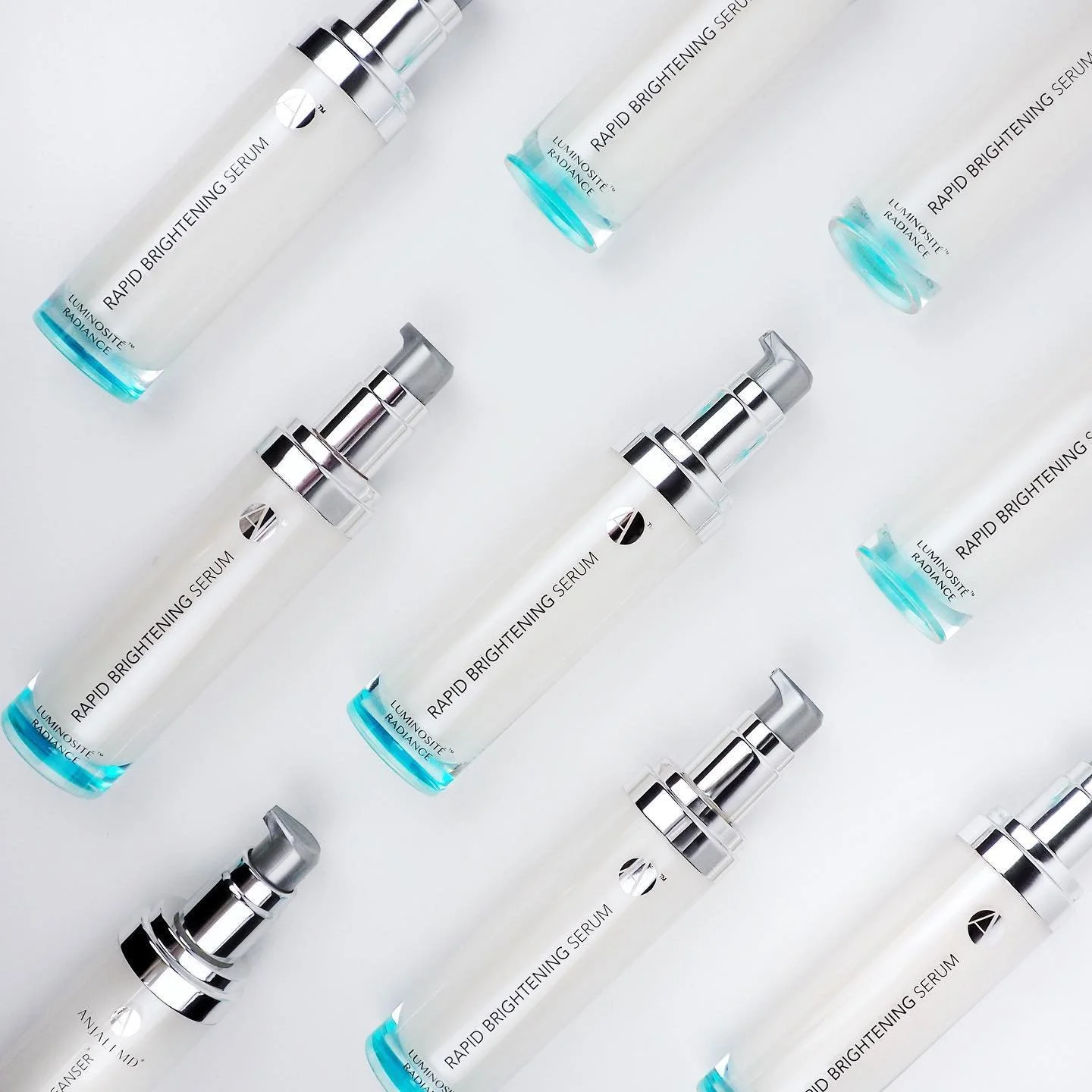 Multiple bottles of luminous skincare serum labeled "Rapid Brightening Serum" arranged on a white background.