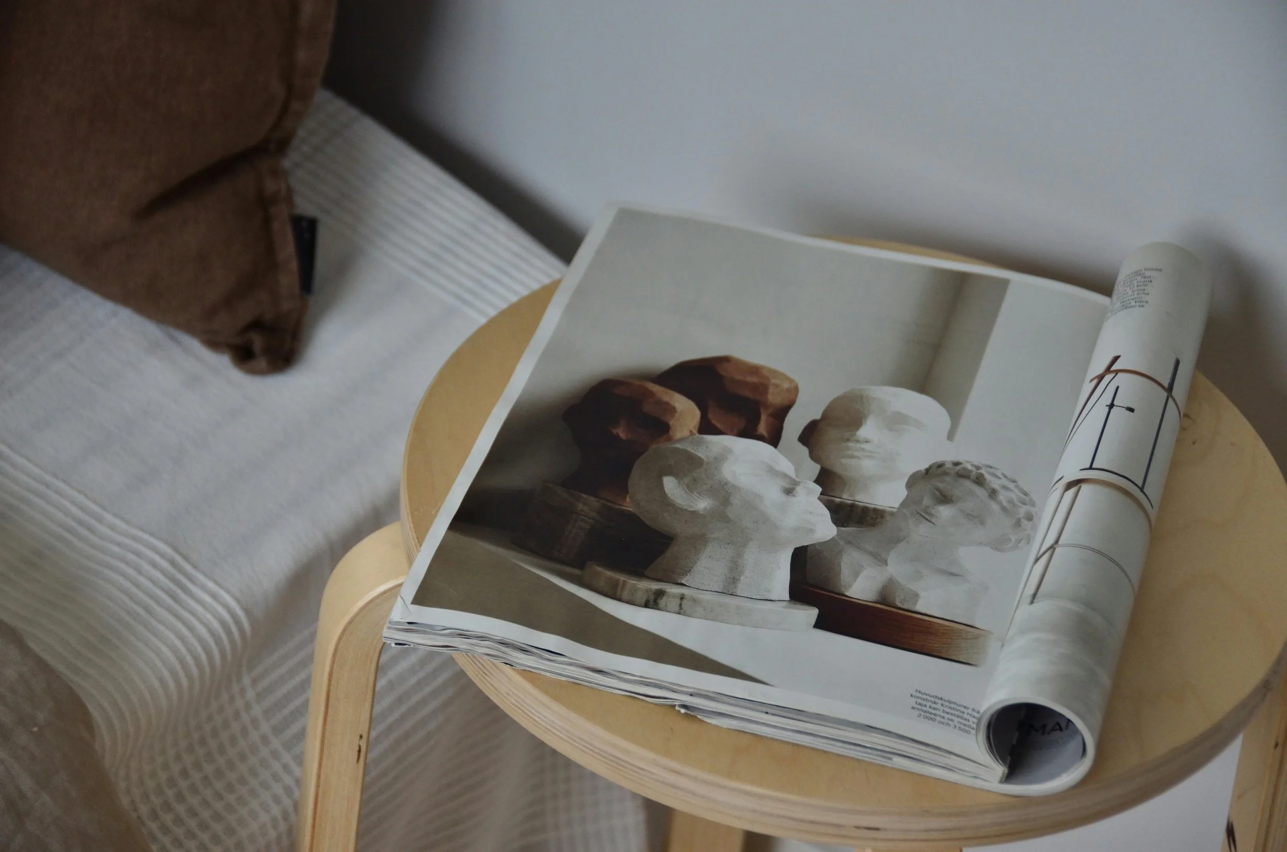 Open magazine on a wooden side table displaying photographs of various sculpted busts and statues.