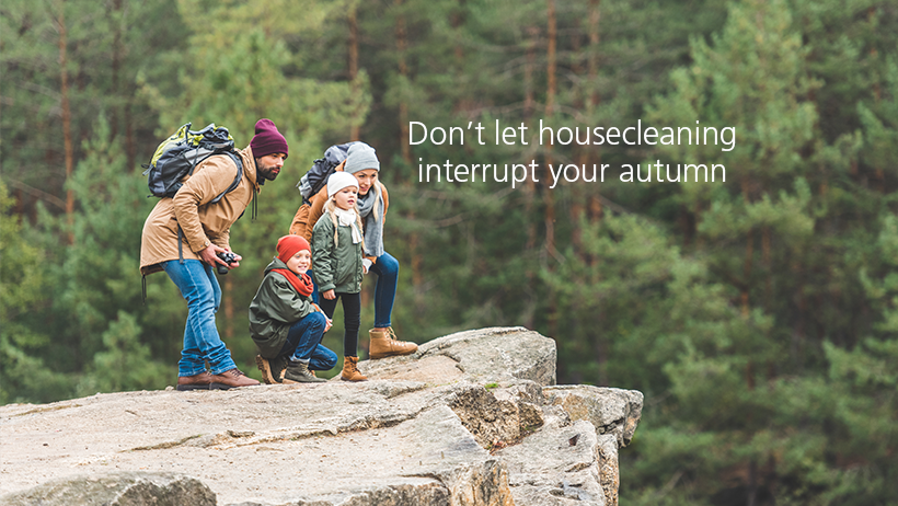 A family of five with backpacks standing on a rocky ledge in a forest, looking out and posing for a photo, with text 'Don’t let housecleaning interrupt your autumn'.