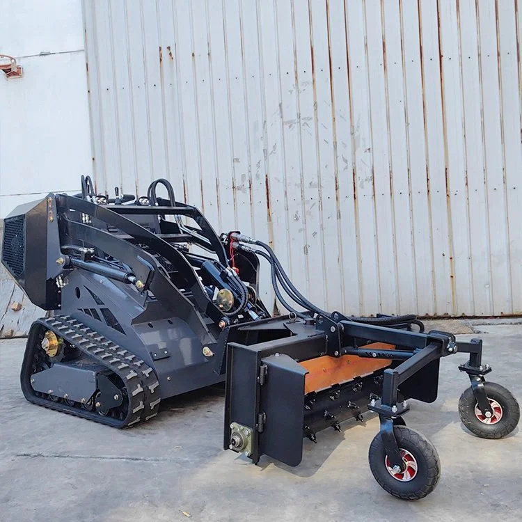Tracked mini skid steer loader with attachment in front of a corrugated metal wall.