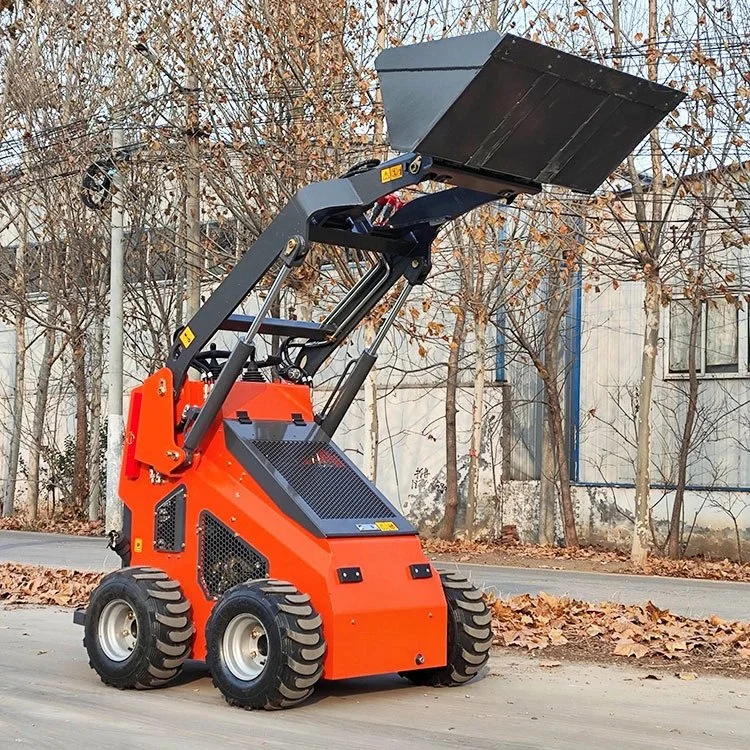 Compact skid steer loader with raised bucket on a street with trees and buildings in the background.
