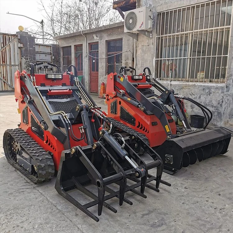 Two red mini skid steer loaders with attachments in an industrial yard.