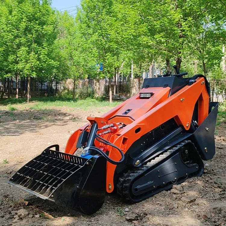 Compact orange skid steer loader on a dirt ground with trees in the background.
