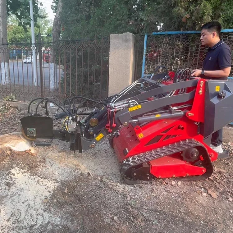Person operating a mini skid steer loader with a stump grinder attachment near a tree stump.