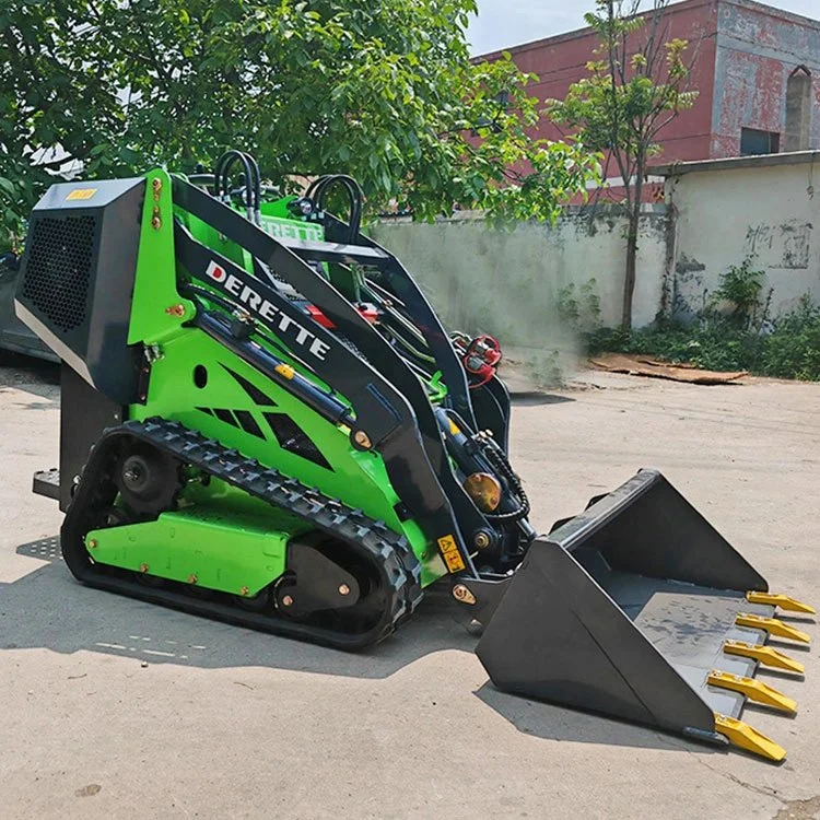 Green mini skid steer loader with tracked wheels and front bucket attachment on pavement, surrounded by trees and building background.