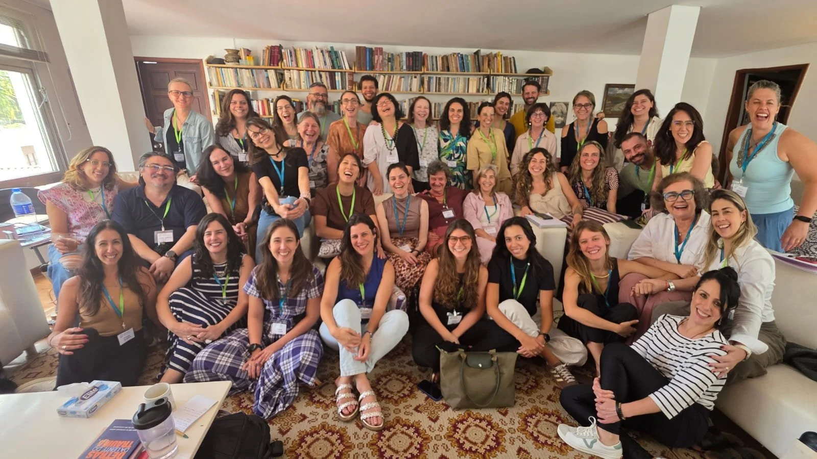 Vários adultos sorrindo e posando para a foto em uma sala com estantes de livros ao fundo.