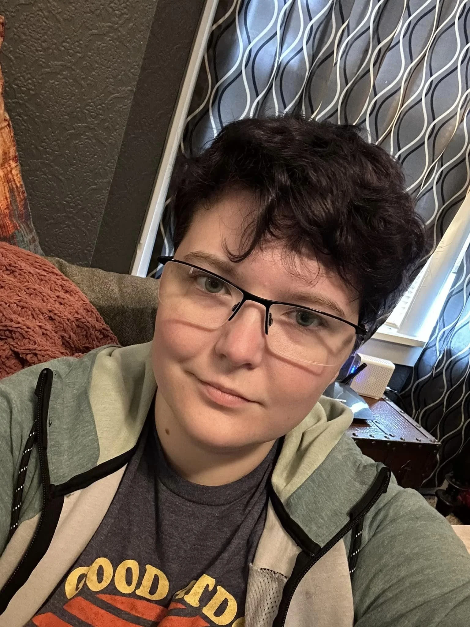 A short brown-haired person with green eyes and partially frameless glasses smiling.