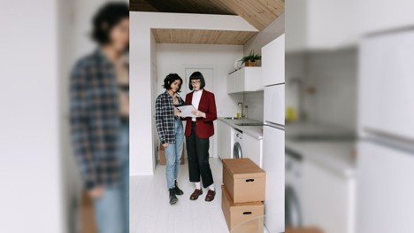 People reviewing housing paperwork in a home with moving boxes while comparing renting and buying decisions.