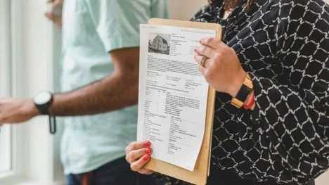 Real estate agent holding property documents on a clipboard during a home tour.