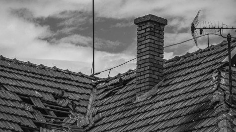 Damaged roof tiles under cloudy skies representing storm and hail damage risk for homeowners insurance.