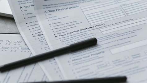 Close-up of a home insurance policy form with pens and a laptop, representing insurance budgeting.