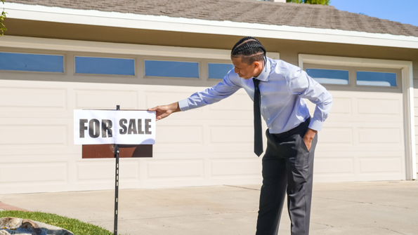 Real estate agent setting up a for sale sign outside a home in a blog about why homes are not selling in Mansfield