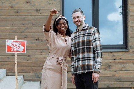 First-time home buyers holding keys near a sold sign for a blog about Mansfield Texas buyer assistance programs.