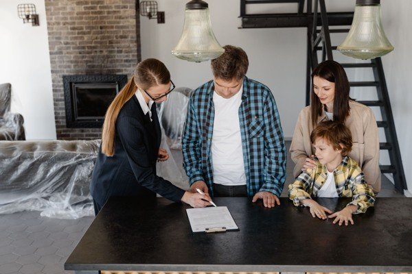Family signing real estate documents with an agent inside a home after qualifying for home buyer assistance.