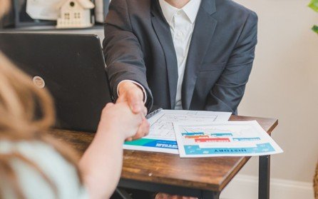 Real estate agent shaking hands with a client over property offer documents.